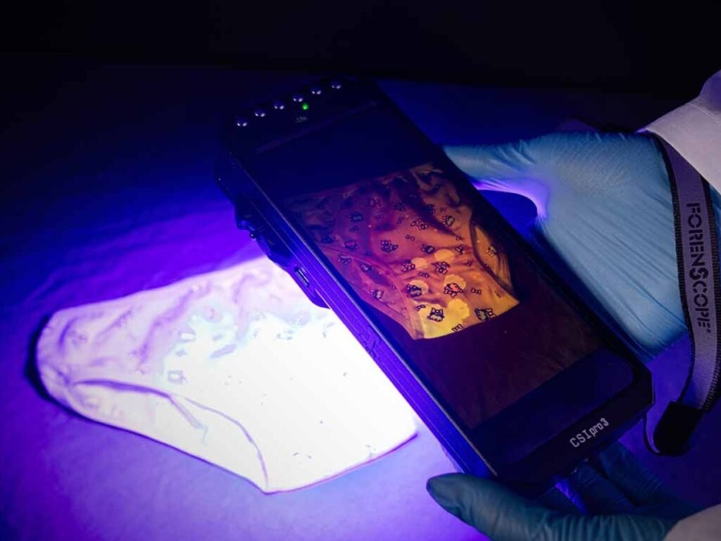 Crime scene technician scanning a surface with the CSI PRO 3 forensic imaging device to detect body fluids and trace evidence during field investigation.