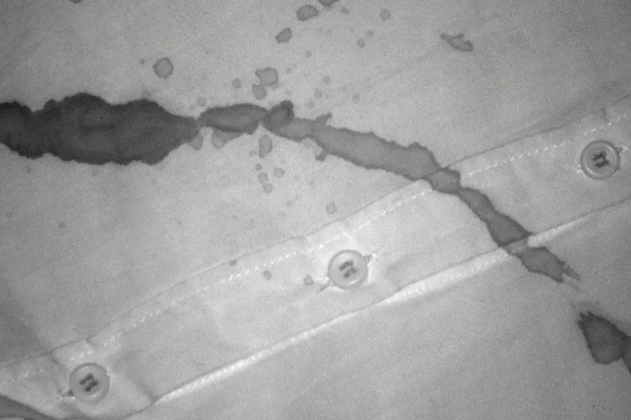 Close-up forensic image showing a blood stain trail and droplets detected across the fabric of a checkered shirt.