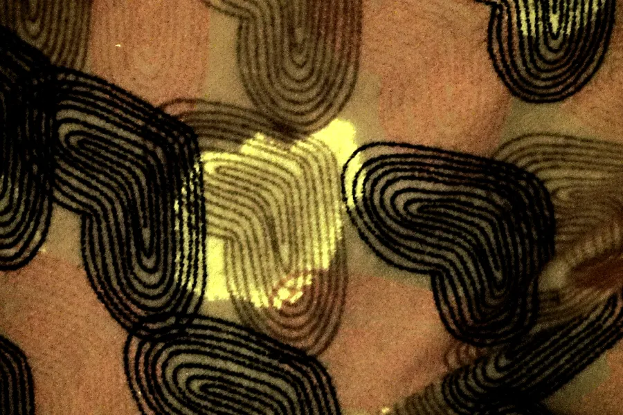 Close-up forensic image showing a fluorescent semen stain detected on the surface of patterned fabric.